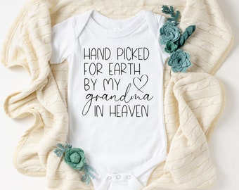 May include: White baby onesie with black text that reads "Hand picked for earth by my grandma in heaven" with a heart symbol.