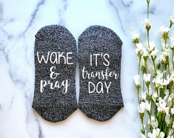 May include: A pair of gray socks with white text. One sock says "Wake & Pray" and the other says "It's Transfer Day".
