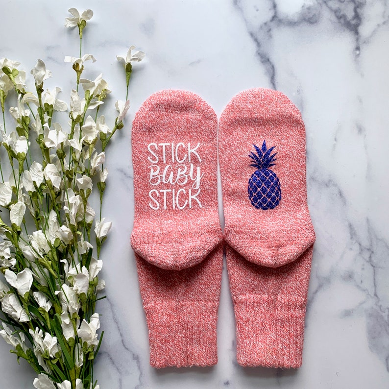 May include: A pair of pink socks with a pineapple design on one sock and the text "STICK BABY STICK" on the other sock.