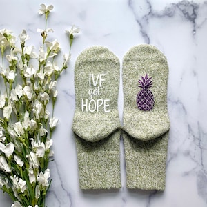 May include: A pair of green socks with white text that says "I've got hope" on one sock and a purple pineapple on the other sock.