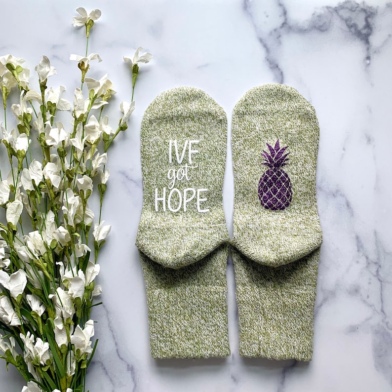 May include: A pair of green socks with white text that says "I've got hope" on one sock and a purple pineapple on the other sock.