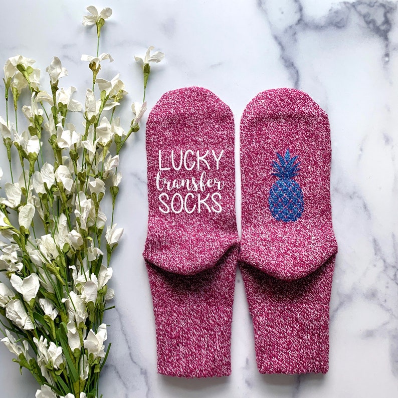 May include: A pair of pink socks with a white pineapple design on one sock and the text "LUCKY transfer SOCKS" on the other sock.