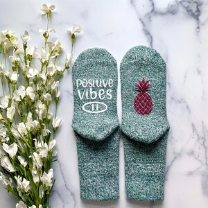 May include: A pair of green socks with a pineapple design and the text "positive vibes" on one sock.
