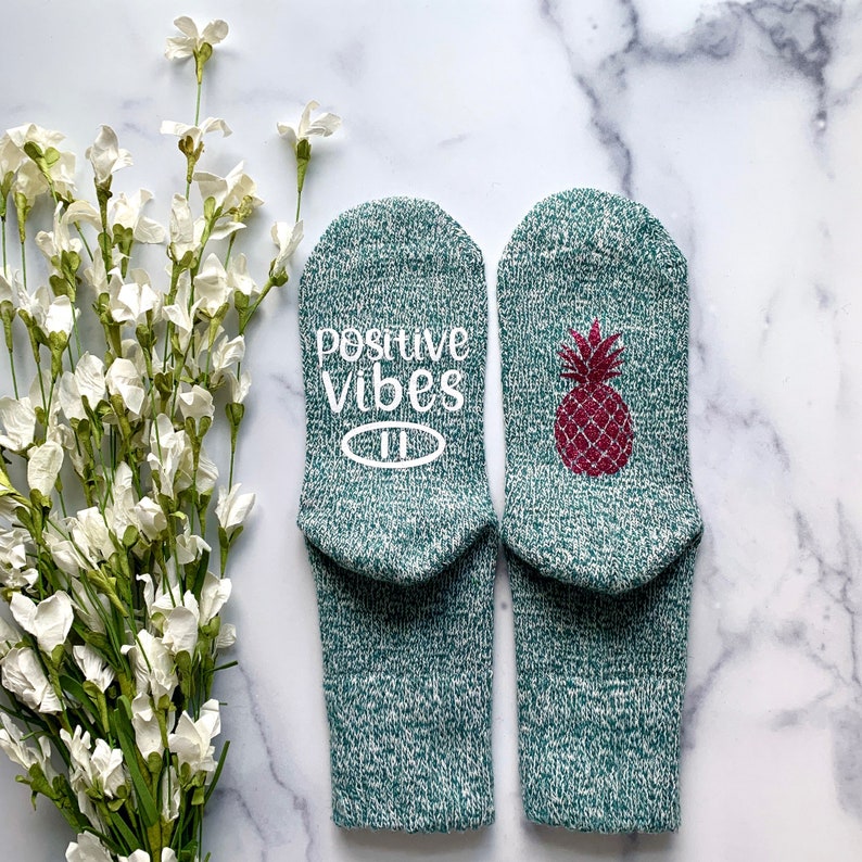 May include: A pair of green socks with a pineapple design and the text "positive vibes" on one sock.