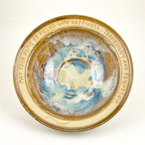 May include: A brown ceramic bowl with a blue and white glaze. The bowl has a rim with the inscription "May your home be filled with happiness, tranquility and friendship."
