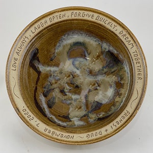 May include: A brown ceramic bowl with a white glaze and a handwritten inscription around the rim that reads "LOVE ALWAYS, LAUGH OFTEN, FORGIVE QUICKLY, DREAM TOGETHER. FRENESI & DOUG NOVEMBER 7, 2020."