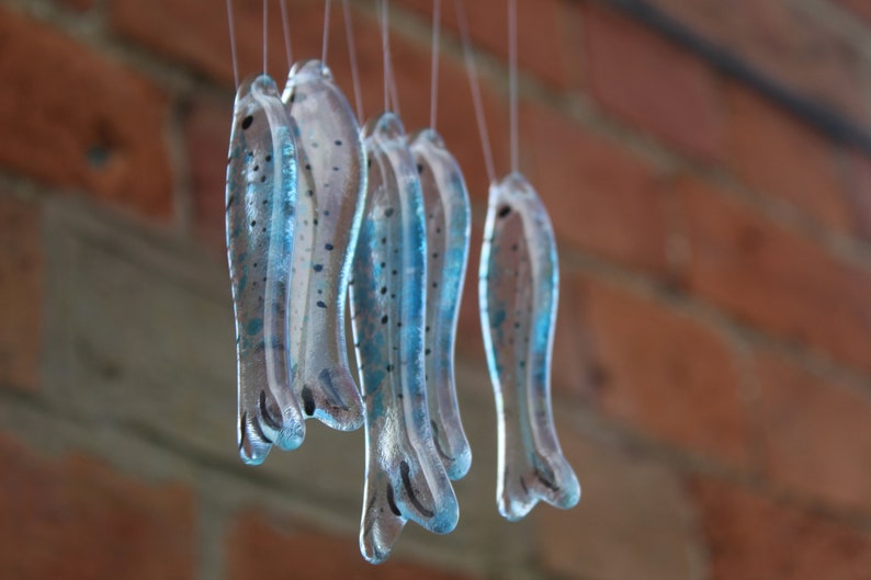 fish wind chimes hanging from driftwood. Fishes made in fused glass and make a lovely wind chime. clear and blue