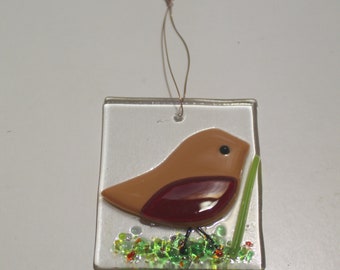 May include: A glass ornament featuring a brown and red bird with a black eye, standing on a bed of green, red, and yellow glass beads. The ornament has a wire loop for hanging.