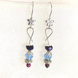 May include: A pair of dangle earrings with silver-tone metal flower accents. Each earring features a loop design, a dark blue bead, a light blue bead, and a small red bead. The earrings are designed for pierced ears.