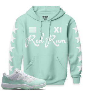 Puede incluir: Una sudadera con capucha verde menta con detalles de estrellas blancas en las mangas y el texto "Red Rum" en escritura blanca. La sudadera tiene un bolsillo delantero y un par de zapatillas a juego.