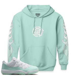 Puede incluir: Una sudadera con capucha verde menta con diseños de llamas blancas en las mangas y un gráfico circular blanco en el pecho. La sudadera con capucha se combina con zapatillas deportivas verdes menta y blancas. La sudadera con capucha tiene el texto "REDRUM NATION" y "FOR SURE ART".