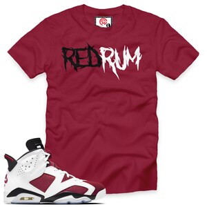 May include: A red t-shirt with the word "REDRUM" printed in black and white letters. A pair of white and burgundy sneakers with black accents.