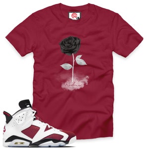 May include: A pair of white and burgundy sneakers with black accents. The sneakers have a black and white rose graphic on the side. The sneakers are next to a red t-shirt with a black rose and the word "Redrum" printed on it.