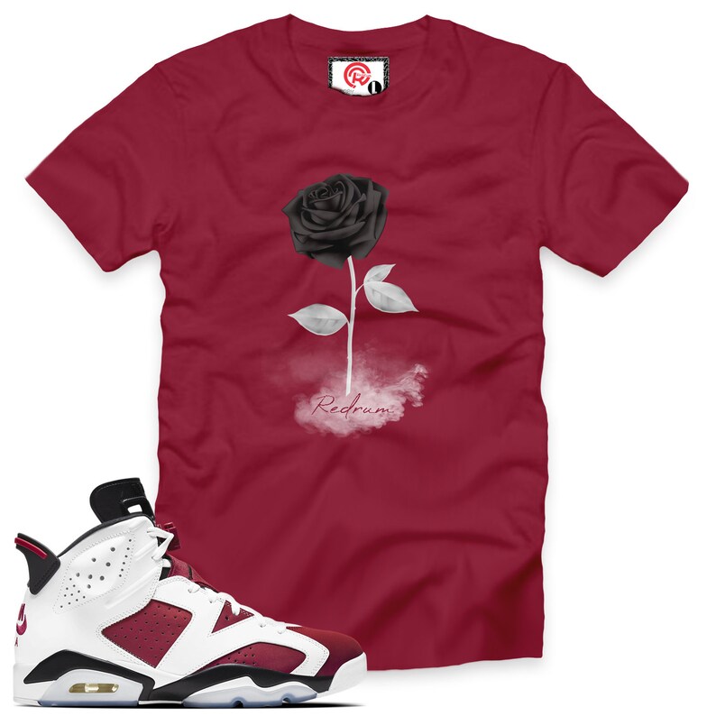 May include: A pair of white and burgundy sneakers with black accents. The sneakers have a black and white rose graphic on the side. The sneakers are next to a red t-shirt with a black rose and the word "Redrum" printed on it.