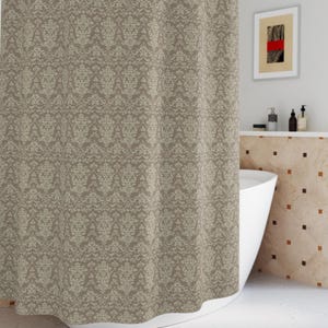 May include: A beige shower curtain with a repeating floral pattern hangs from a curved, silver-colored shower rod. The curtain is the focal point in a bathroom setting, with a white bathtub and a small framed artwork visible.