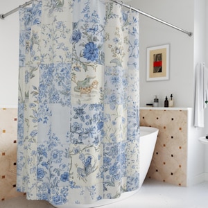 May include: A patchwork shower curtain featuring a floral design in blue and white. The curtain is suspended from a curved, chrome-effect rail. The bathroom includes a white bathtub, a small table, and framed artwork.