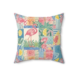 May include: Square cushion with a patchwork design featuring pink flamingos, lemons, flowers, and tropical foliage. The cushion has a white background with blue, pink, yellow, and green accents. A decorative item for a living room or bedroom.