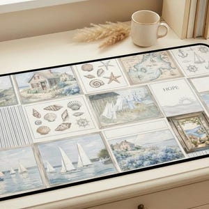 May include: A rectangular desk mat with a nautical theme. The mat features a collage of watercolour illustrations including sailboats, seashells, maps, and coastal scenes. The colour palette includes blues, whites, and beige, with a black border.