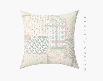 May include: Square decorative pillow with a patchwork design. The pillow features various floral and patterned fabrics in soft pastel colors, including pink, green, and cream. The pillow is a square shape.