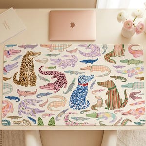 May include: A desk mat featuring a colorful pattern of various crocodiles and alligators. The design includes a leopard-print crocodile, a blue spotted dog-like crocodile, and other whimsical illustrations. A laptop and flowers are also on the desk.