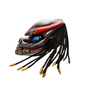 Pu&ograve; includere: Un casco da moto con un design Predator. Il casco presenta una combinazione di colori rosso e argento, con dreadlocks neri e punte dorate. La visiera &egrave; blu e il casco ha un aspetto dettagliato e strutturato.