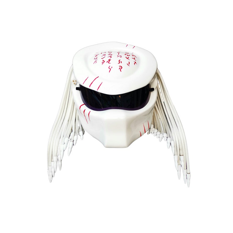 May include: White motorcycle helmet with a Predator design. The helmet features a smooth, glossy finish, dark visor, and red accents. It has white dreadlocks and a unique, angular shape, perfect for cosplay or themed events.