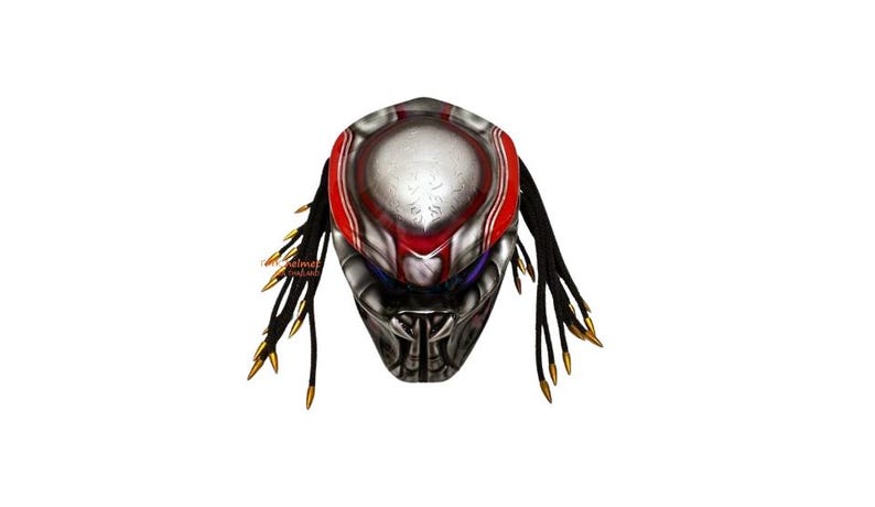 Pu&ograve; includere: Una maschera di Predator dettagliata con una combinazione di colori argento metallizzato, rosso e nero. La maschera presenta dettagli intricati, tra cui una sezione centrale argentata con accenti rossi e dreadlocks neri con punte dorate.