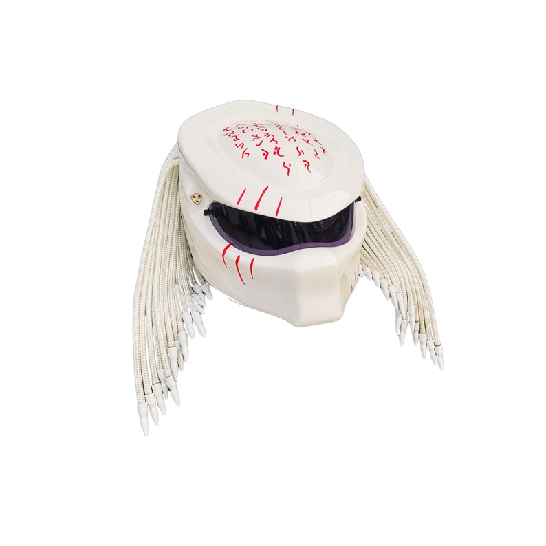 May include: A white motorcycle helmet with a Predator design. The helmet features a dark visor, red markings, and white dreadlocks. The top of the helmet has red markings and a gold emblem.
