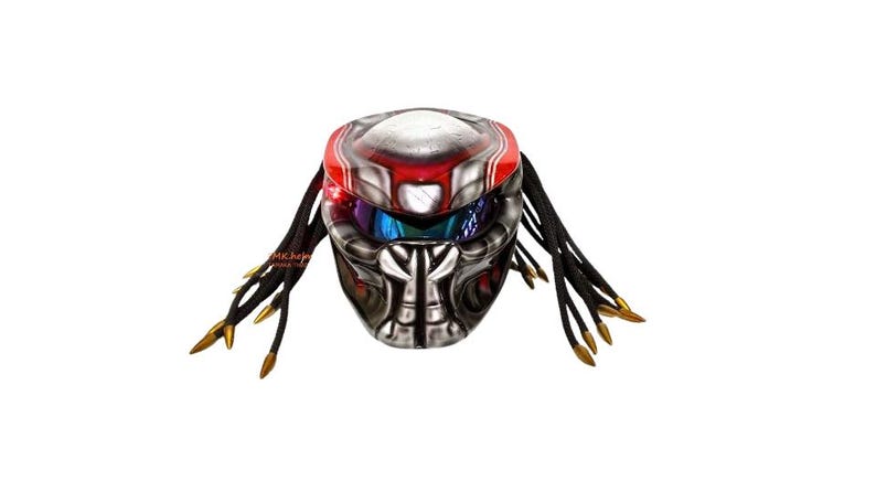 Pu&ograve; includere: Un casco da moto a tema Predator con finitura argento e nero metallizzato, accentuato da strisce rosse e una visiera riflettente. Il casco presenta viticci simili a dreadlock con punte dorate.