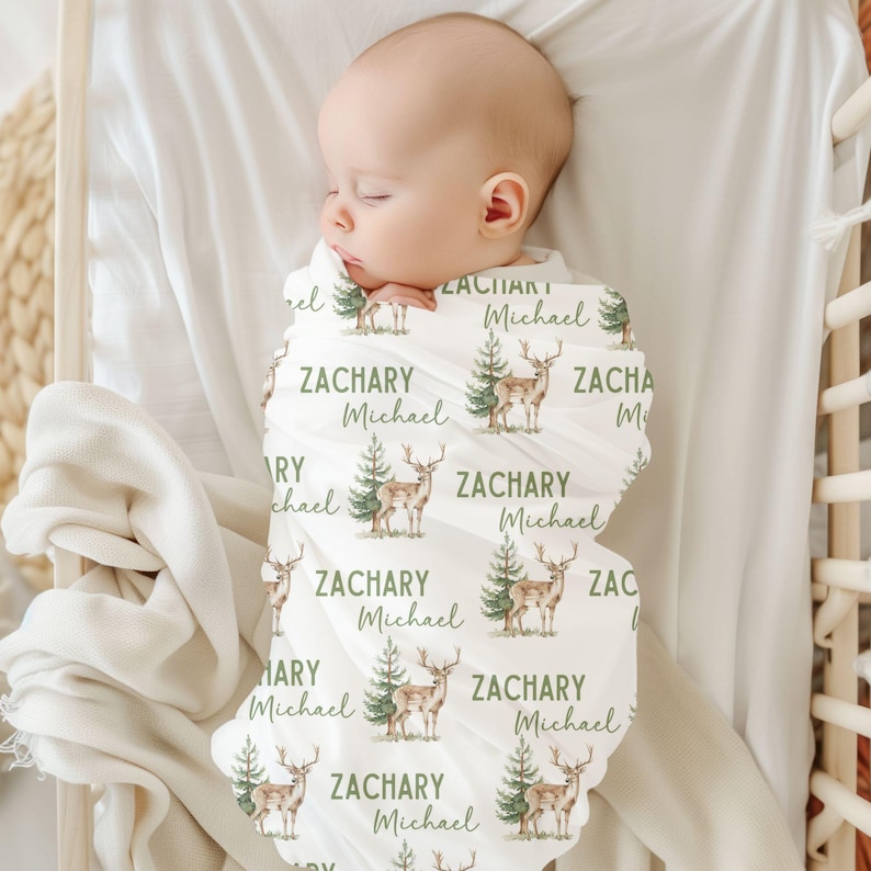 May include: A white swaddle blanket with a repeating pattern of green trees and brown deer. The blanket is personalized with the name "Zachary Michael" repeated throughout the design.