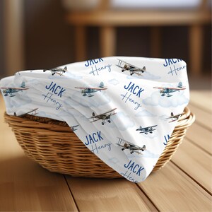 May include: White baby blanket with a blue airplane pattern and the name "Jack Henry" repeated throughout.