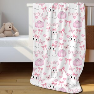 May include: Pink and white baby blanket with a ghost and pumpkin pattern. The blanket has the name "Brinley" repeated throughout the design.