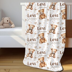 May include: White baby blanket with a repeating pattern of brown teddy bears wearing brown bow ties. The blanket has a light brown polka dot pattern and brown bows. The text "Levi Jameson" is repeated throughout the blanket.
