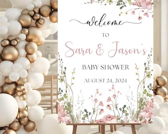 May include: A white welcome sign with pink floral accents and greenery. The sign reads "Welcome to Sara & Jason's Baby Shower August 24, 2024".