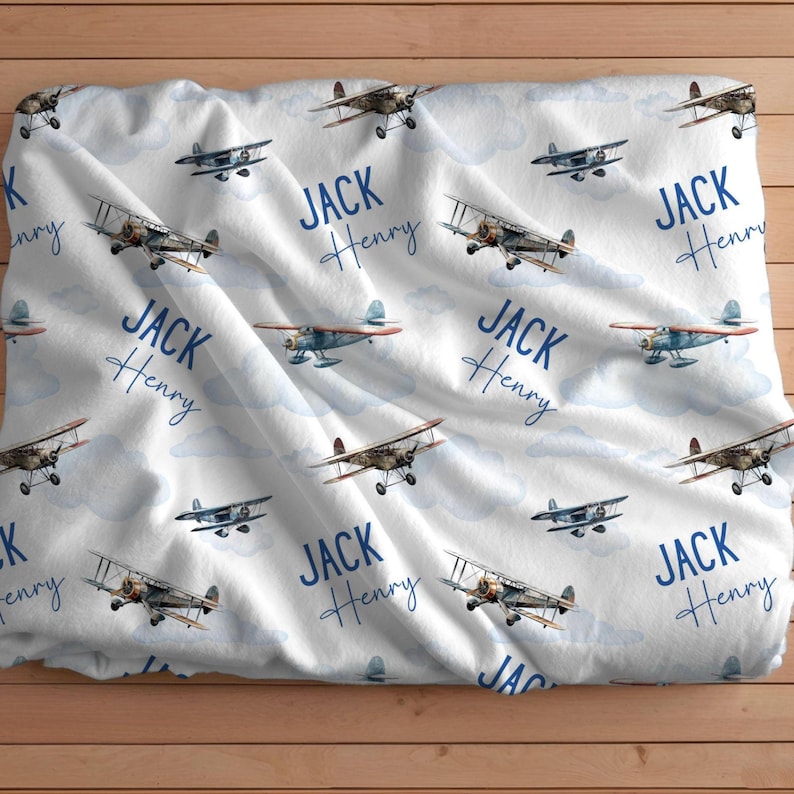 May include: White baby blanket with a blue airplane pattern. The blanket has the name "JACK HENRY" repeated throughout the design.