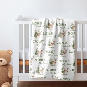 May include: White baby blanket with a repeating pattern of green trees and brown deer. The blanket has the names "Zachary" and "Michael" printed on it.