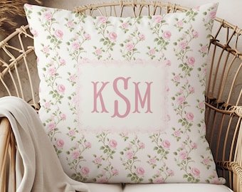 Può includere: Un cuscino bianco con un motivo floreale rosa e un monogramma rosa che dice "KSM".