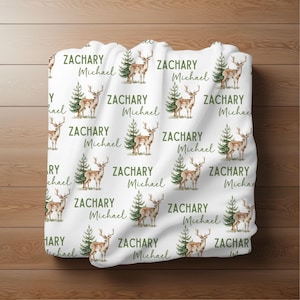 May include: White fabric with a repeating pattern of a brown deer standing in front of a green pine tree. The text "Zachary Michael" is repeated throughout the fabric.