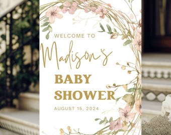 May include: A white welcome sign with a floral wreath design in shades of pink and green. The text "Welcome to Madison's Baby Shower August 15, 2024" is written in gold.