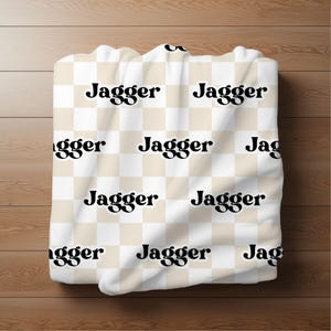 K&ouml;nnte beinhalten: Wei&szlig;er und beiger karierter Stoff mit dem Wort "Jagger" in schwarzer Retro-Schrift wiederholt.