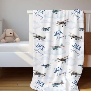 May include: A white baby blanket with a blue and white airplane pattern. The blanket features the names "Jack Henry" repeated throughout the design.