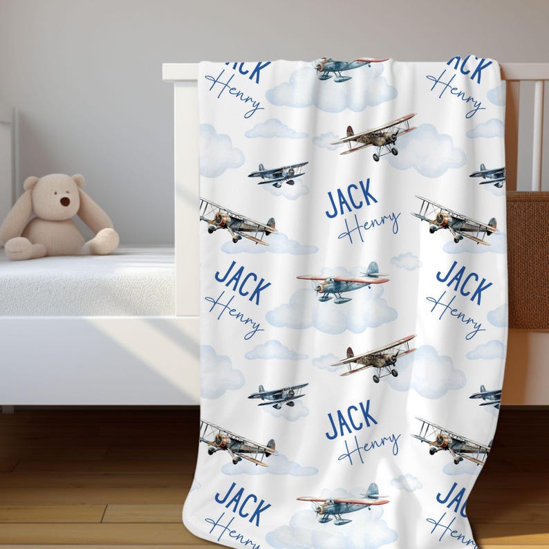 May include: A white baby blanket with a blue and white airplane pattern. The blanket features the names "Jack Henry" repeated throughout the design.
