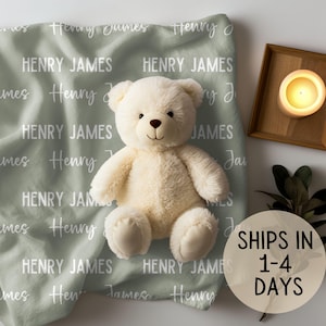 May include: A sage green baby blanket with the names "Henry James" repeated in white script. A white teddy bear sits on the blanket.