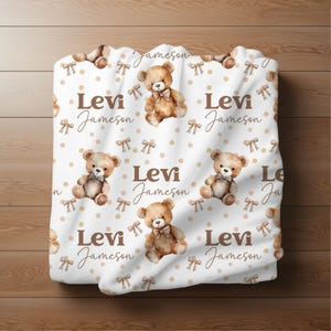 May include: White baby blanket with a repeating pattern of brown teddy bears wearing brown bows, brown polka dots, and the text "Levi Jameson" in brown.