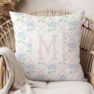 May include: A white pillow with a pink and blue floral pattern and a pink letter "M" in the center.