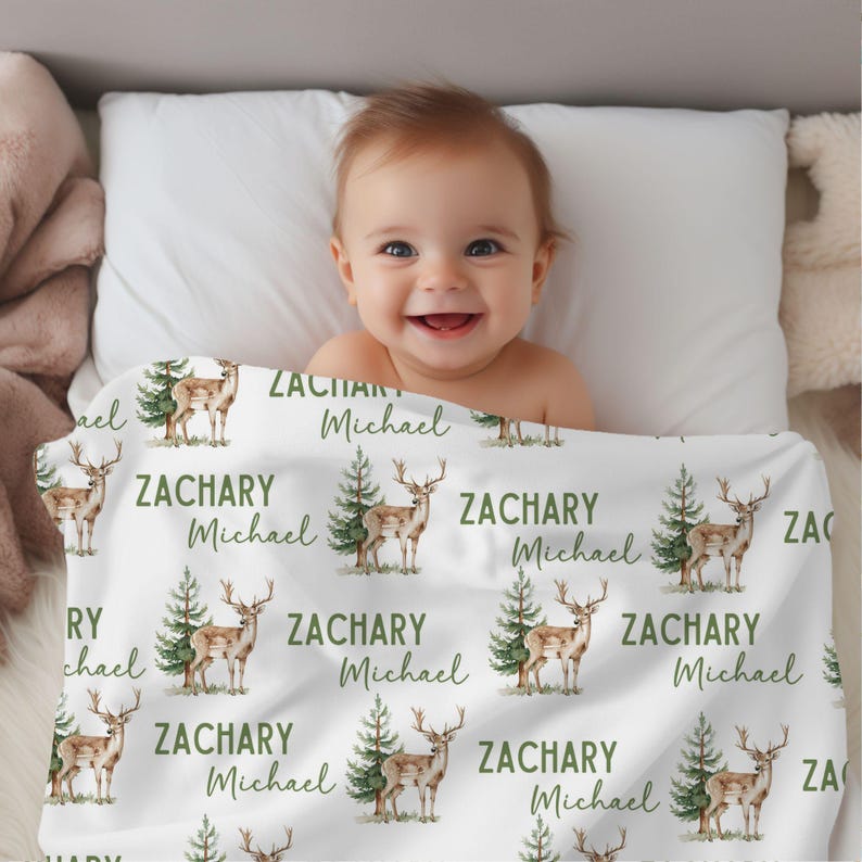 May include: A white baby blanket with a repeating pattern of green trees and brown deer. The blanket has the name "Zachary Michael" printed on it.
