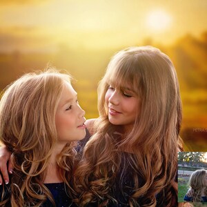 May include: Two young girls with long blonde hair are looking at each other. The girl on the left has her arm around the girl on the right. They are both wearing blue dresses. The background is a blurred image of a sunset.