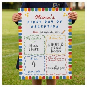 May include: A white rectangular sign with a colourful border of red, yellow, blue, and green segments. The text reads: Olivia's FIRST DAY OF RECEPTION, Date 1st September 2026, My teacher is Miss Clark, I love to paint & read books, I am 4 years old, When I grow up I want to be a Firefighter.