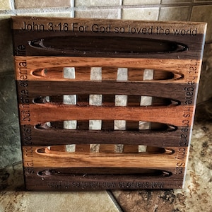 May include: Wooden hot pad with a light brown, dark brown, and black wood design. The hot pad has a quote from the Bible, John 3:16, "For God so loved the world that he gave His one and only Son, that everyone who believes in Him shall not perish but have eternal life."