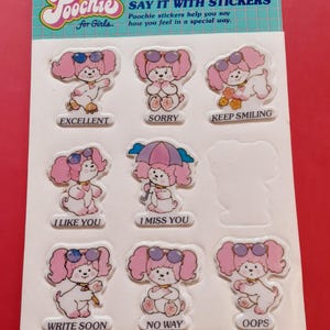May include: Sheet of vintage Poochie stickers for girls. The stickers feature a pink cartoon dog with sunglasses in various poses, with phrases like "Excellent," "Sorry," and "Keep Smiling." The packaging includes the text "Say it with Stickers."